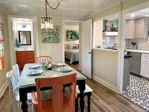 A dining area with a table set for four, a chandelier, and a view into a bedroom.