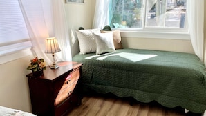 Une chambre avec un lit simple, une table de chevet avec une lampe et une fenêtre donnant sur l’extérieur.