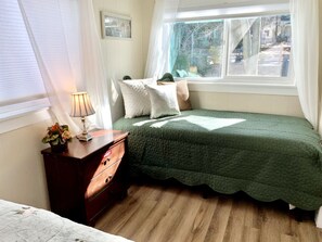 Une chambre avec un lit simple, une table de chevet avec une lampe et une fenêtre donnant sur l’extérieur.