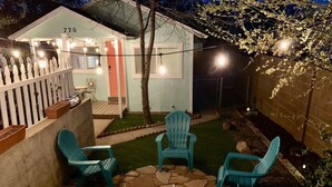 En baghave med en terrasse, fire stole og et bord, omgivet af et hvidt stakittet hegn og et lille skur med nummer 720.