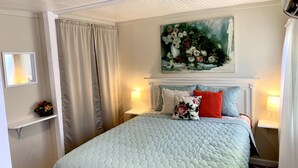 Une chambre à coucher bien rangée, avec un lit, deux lampes de chevet, un tableau au-dessus du lit et une étagère sur laquelle est posé un vase.