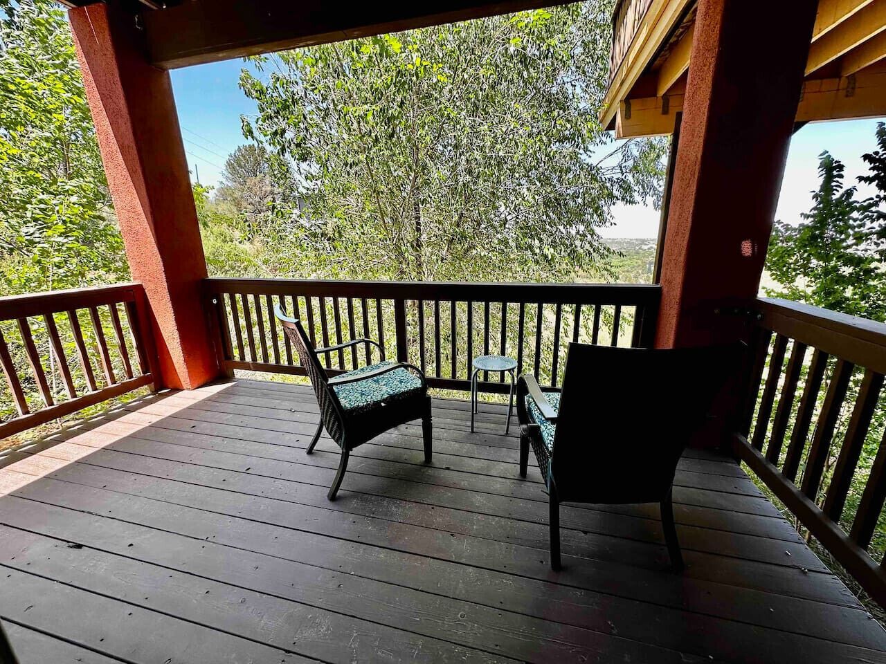 A wooden deck with two chairs and a small table, surrounded by a railing.