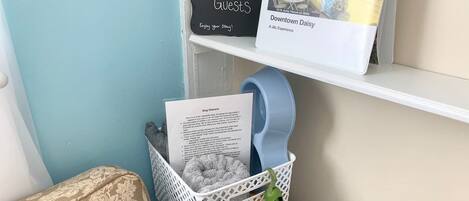 A corner of a room with a welcome sign, a framed photo, a basket with a dog leash, and a dog owner’s notice.