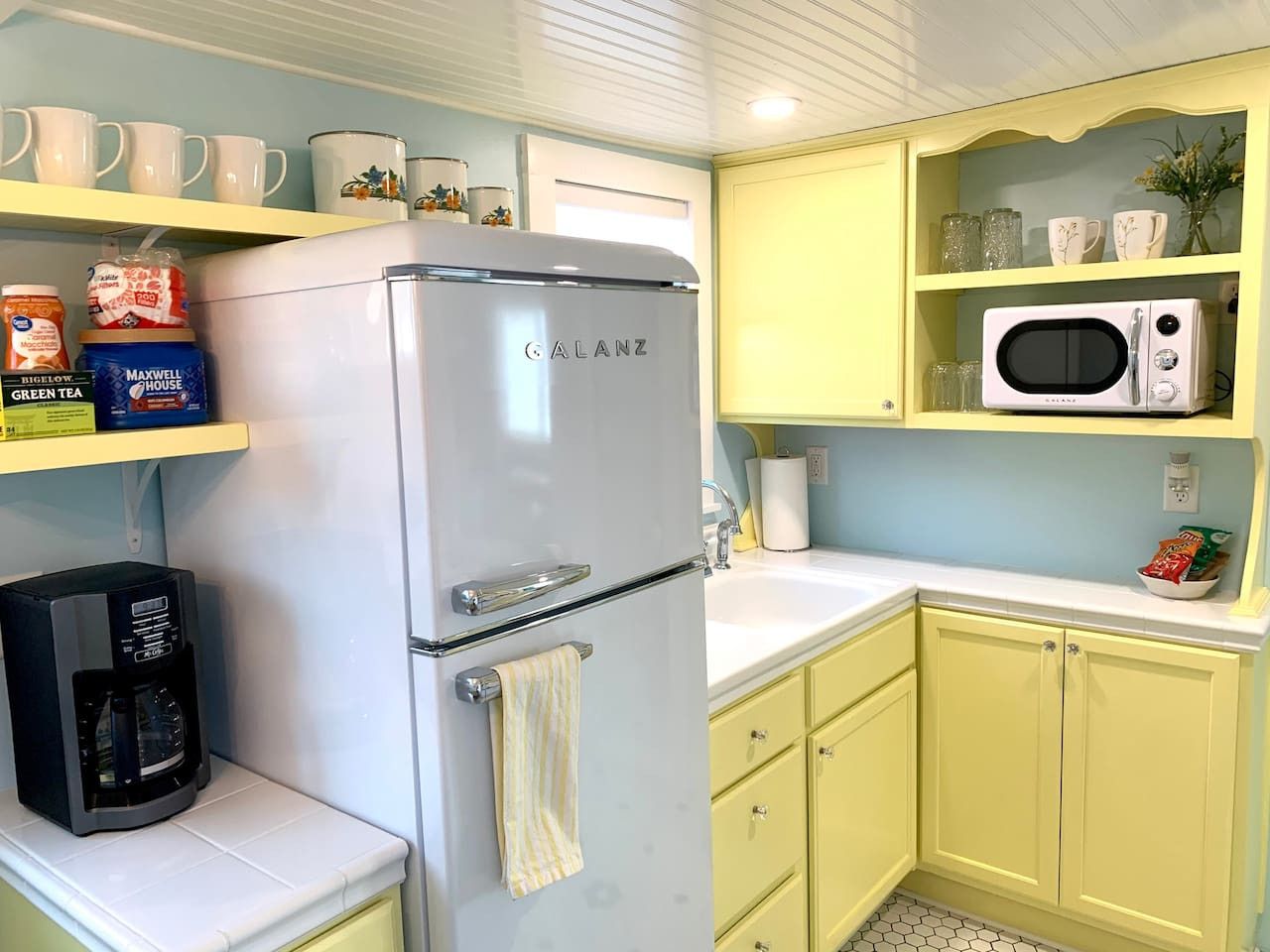 A compact kitchen with a white refrigerator, a coffee maker, and a microwave on a yellow countertop.