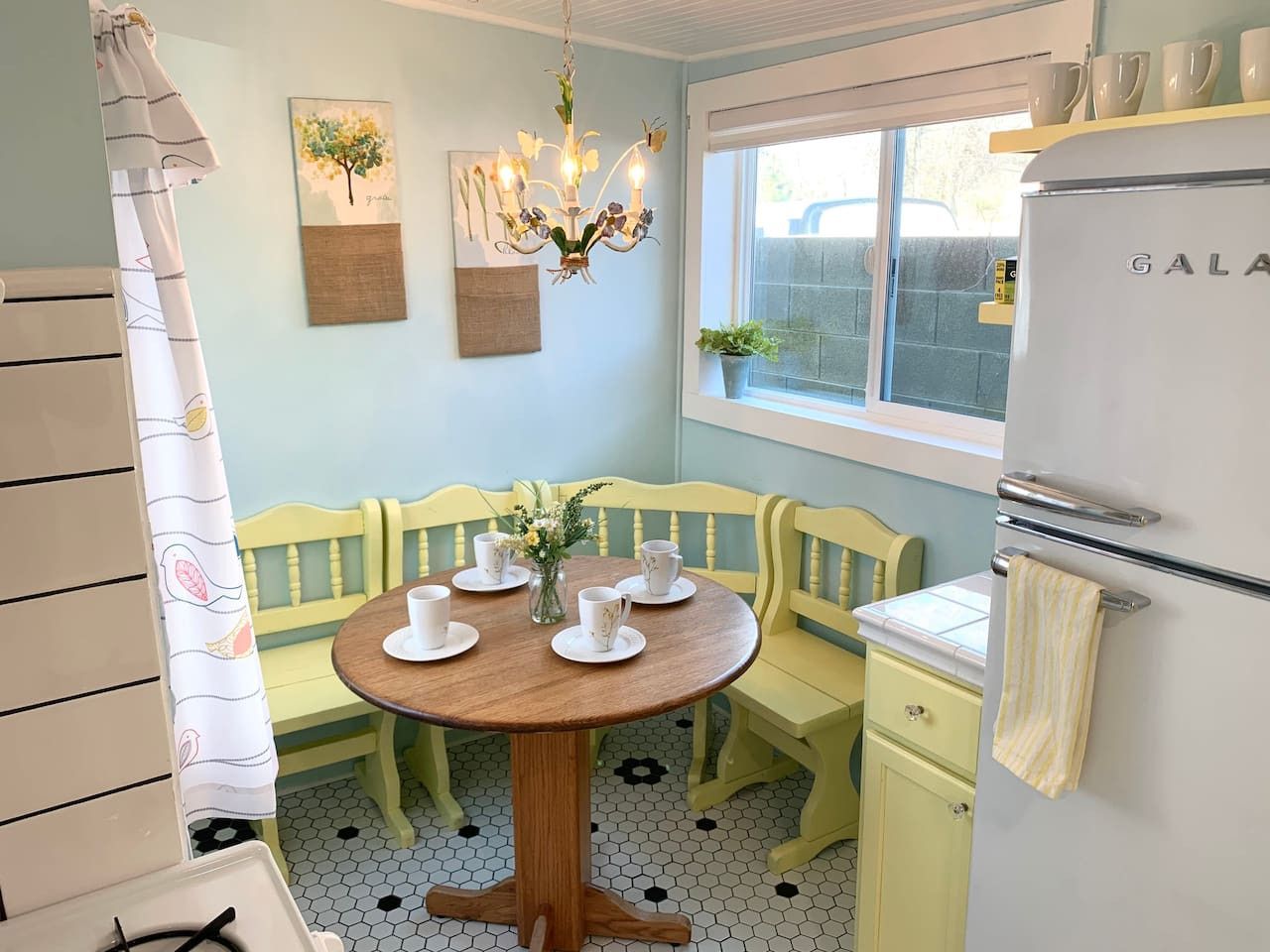 Una cocina con una mesa redonda de madera, sillas amarillas, un refrigerador blanco y una ventana con vistas.