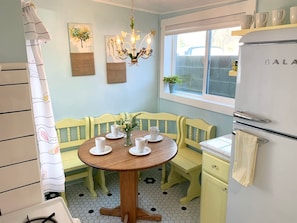 Una cocina con una mesa redonda de madera, sillas amarillas, un refrigerador blanco y una ventana con vistas.