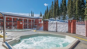 Ein Whirlpoolbereich mit Pool, umgeben von einem roten Gebäude, einem verschneiten Zaun und Bäumen im Hintergrund.