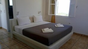 A clean, well-lit hotel room with a large bed, two pillows, and neatly folded towels on the bed. - fira Blue Horizon (Santorini)