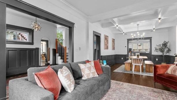 A spacious living room with a grey sofa, red and beige cushions, a dining area with a wooden table and chairs, and a kitchen in the background. - Walnut Charming Modern 5BR Home Walkable Kings (Kansas City)