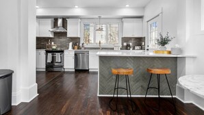 A modern kitchen with white cabinets, a stainless steel range, and a large island with bar stools. - Walnut Charming Modern 5BR Home Walkable Kings (Kansas City)