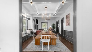 A spacious dining area with a long wooden table, white chairs, and a chandelier. - Walnut Charming Modern 5BR Home Walkable Kings (Kansas City)