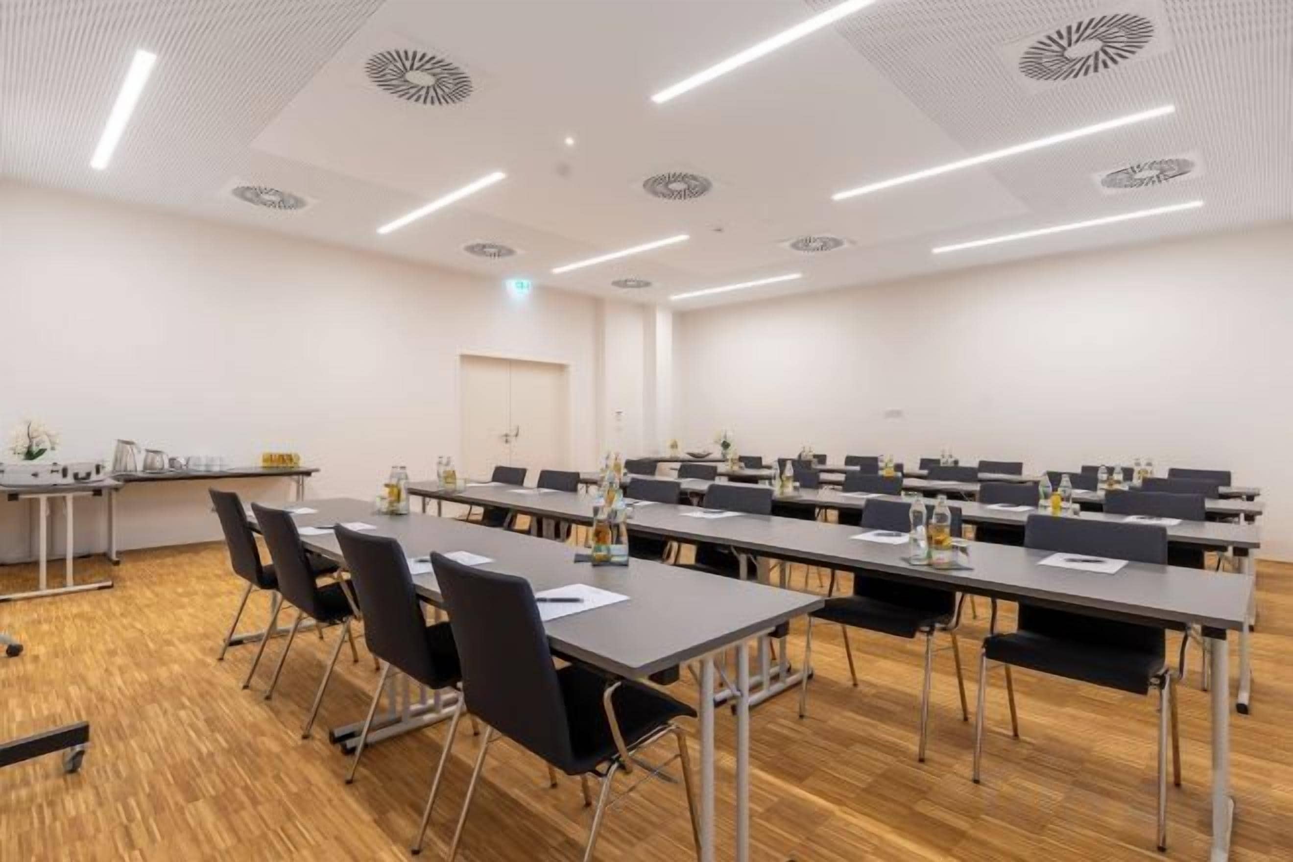 A conference room with multiple tables and chairs, a wooden floor, and a white ceiling with circular patterns.