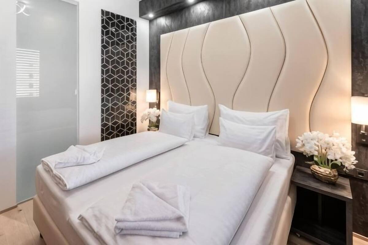 Ein Hotelzimmer mit einem großen Bett, einem Kopfteil, einem Nachttisch mit Lampe und einer Wand mit geometrischem Muster.