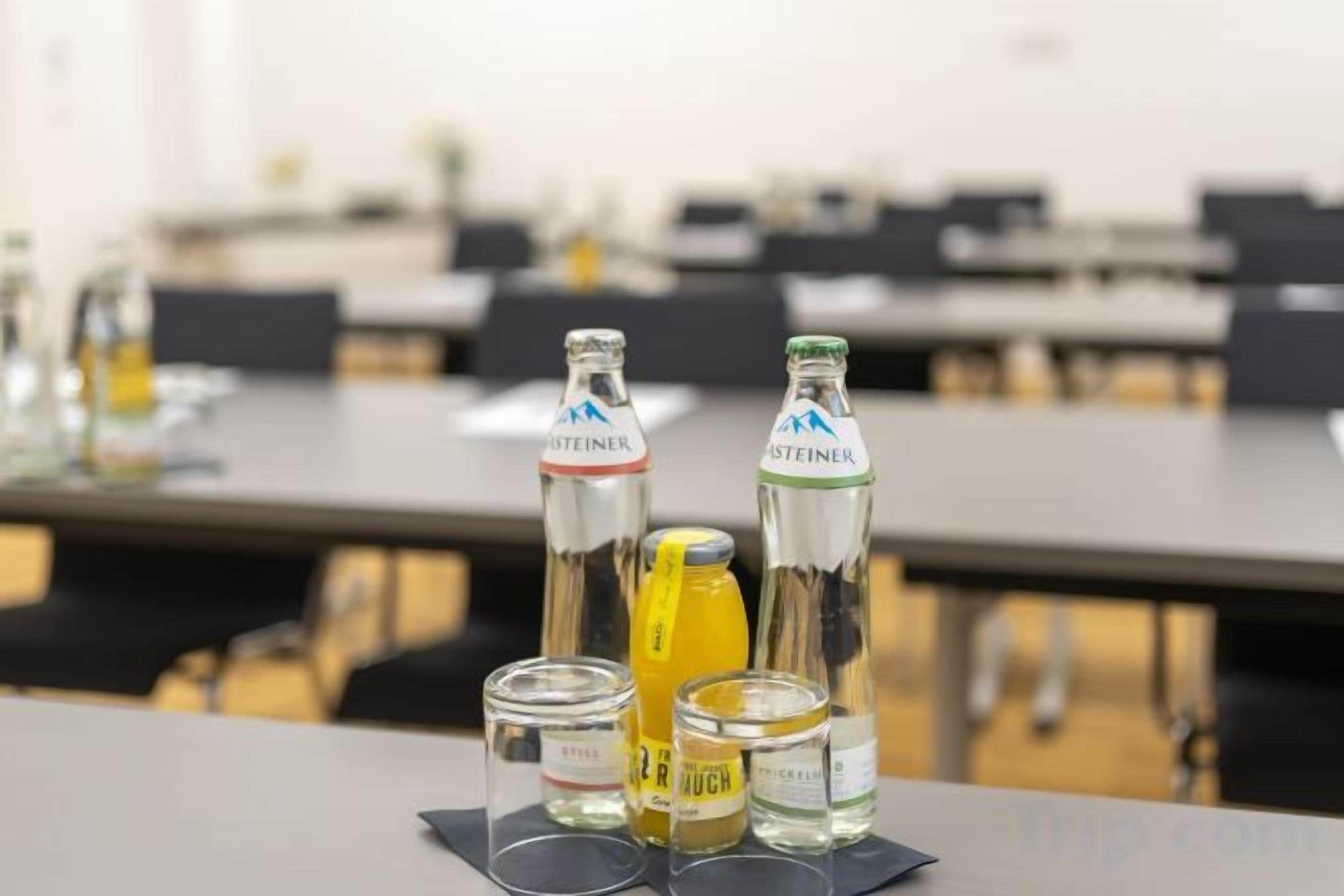 Sala de conferência com mesas, cadeiras, garrafas de água e um copo de suco na mesa.