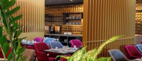 Interior de restaurante con mesas, sillas, un panel de madera y una pared con estanterías.