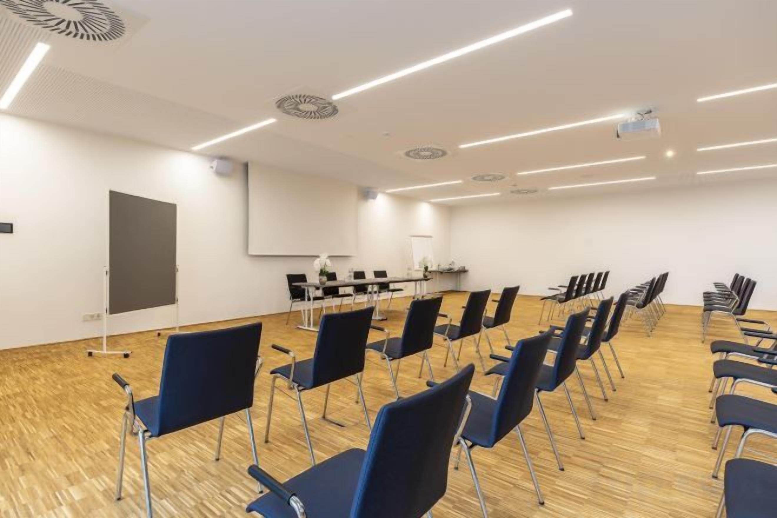A conference room with rows of chairs, a projector screen, and a whiteboard.