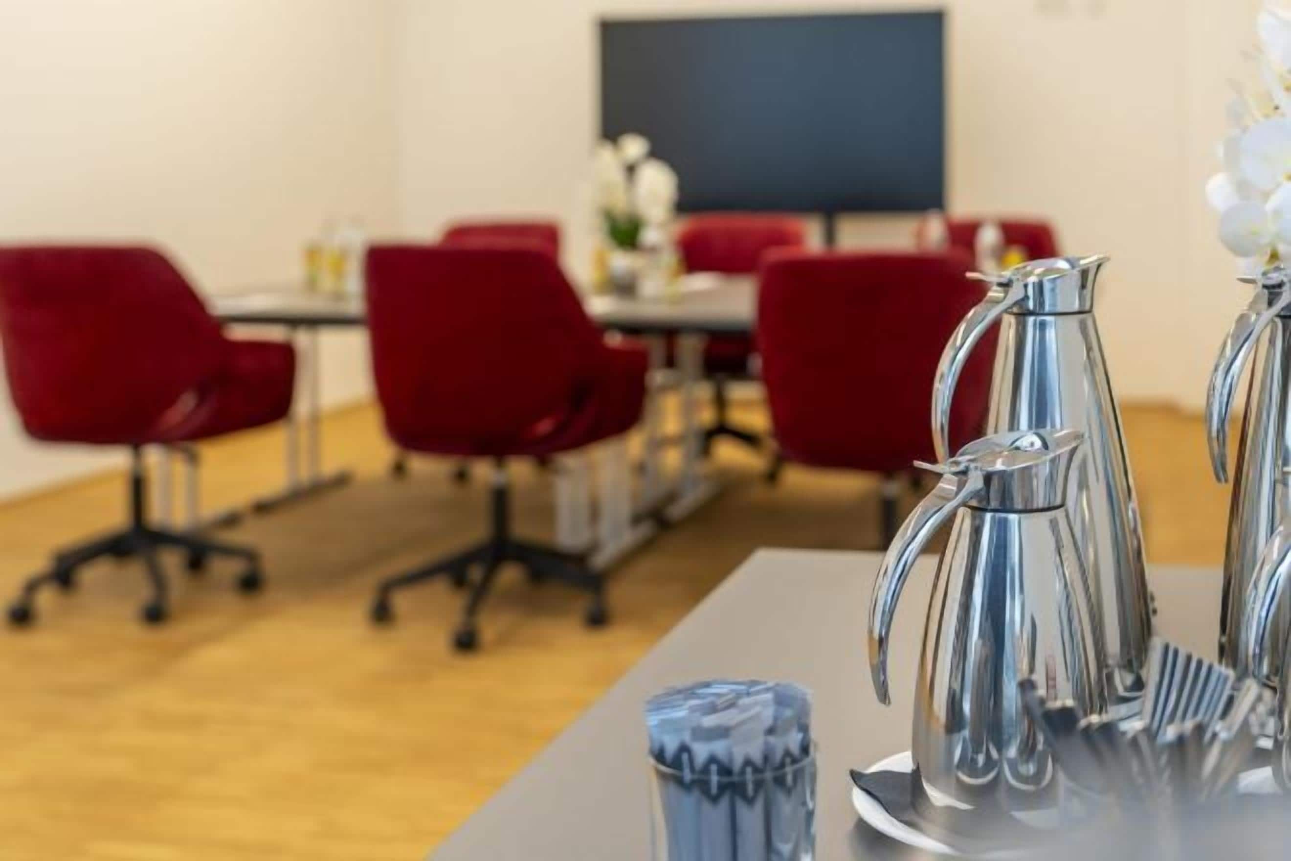 A conference room with red chairs, a table with a silver pitcher, and a blue vase.