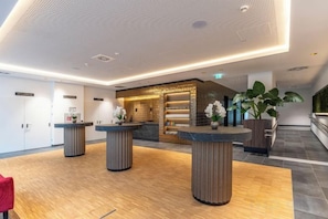 A modern hotel lobby with reception counters, a reception desk, and a large potted plant. - PLAZA INN Wiener Neustadt (Wiener Neustadt)