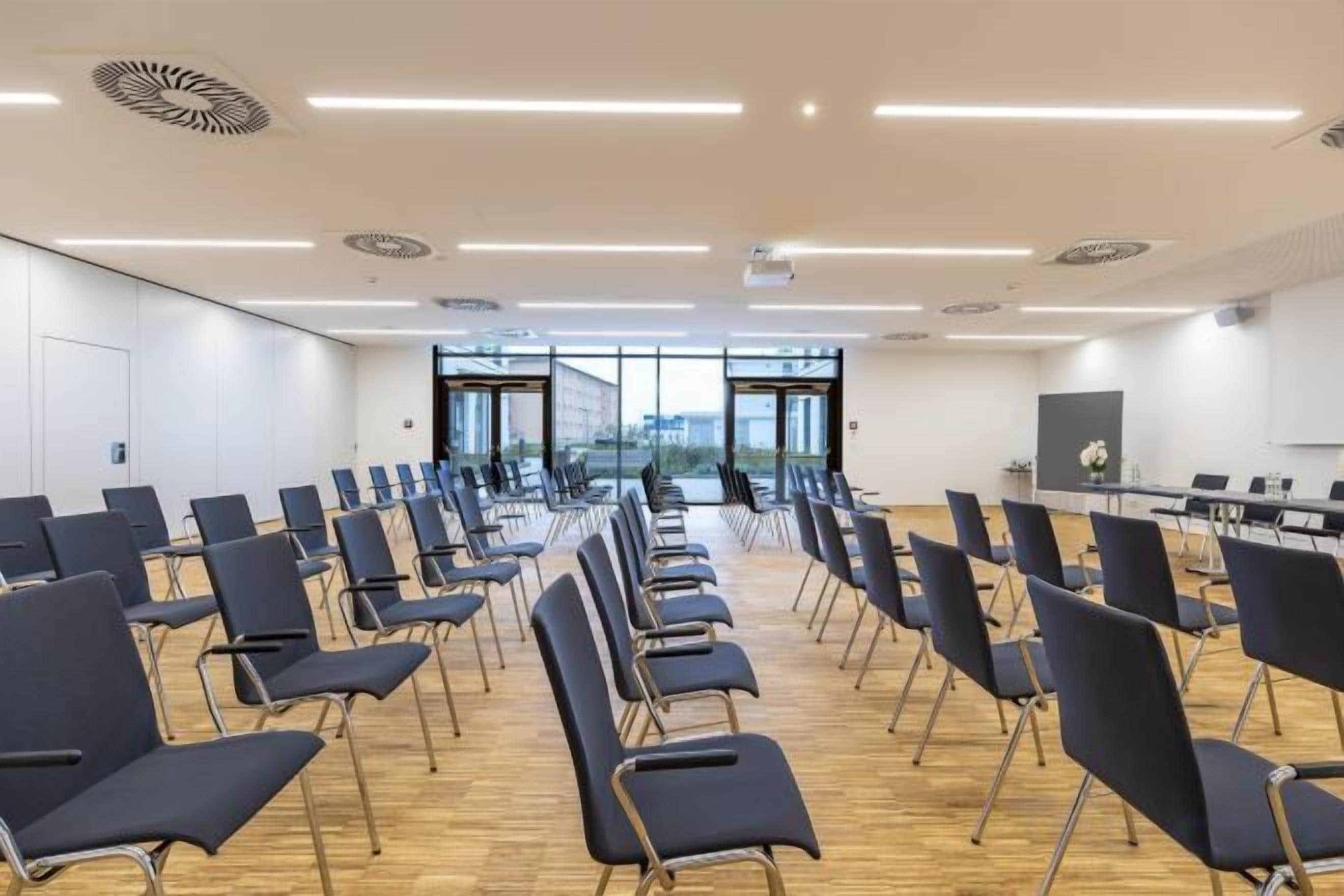 A conference room with rows of chairs, a long table, and large windows.