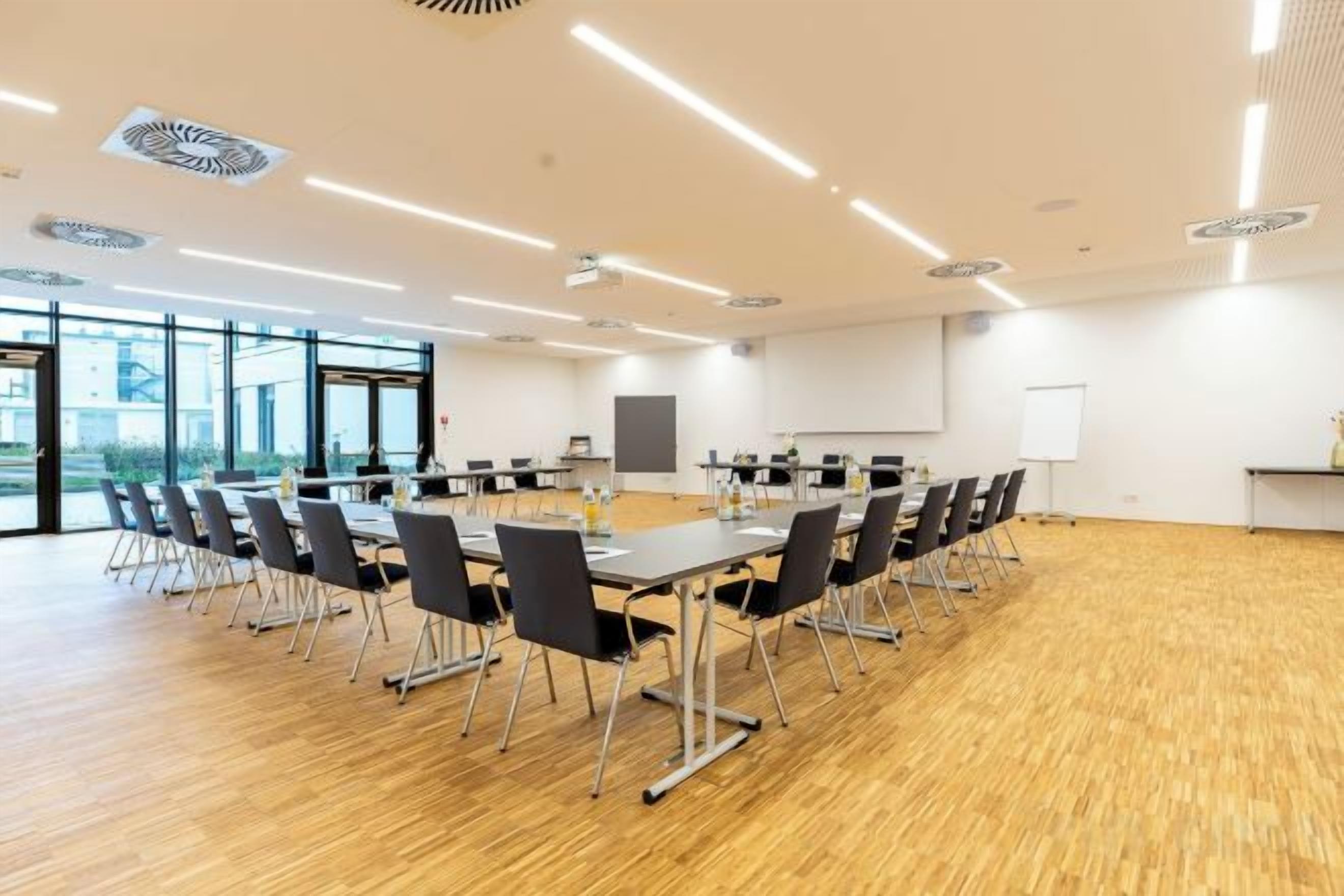 Een vergaderzaal met een lange tafel, stoelen, een projectiescherm en een whiteboard.