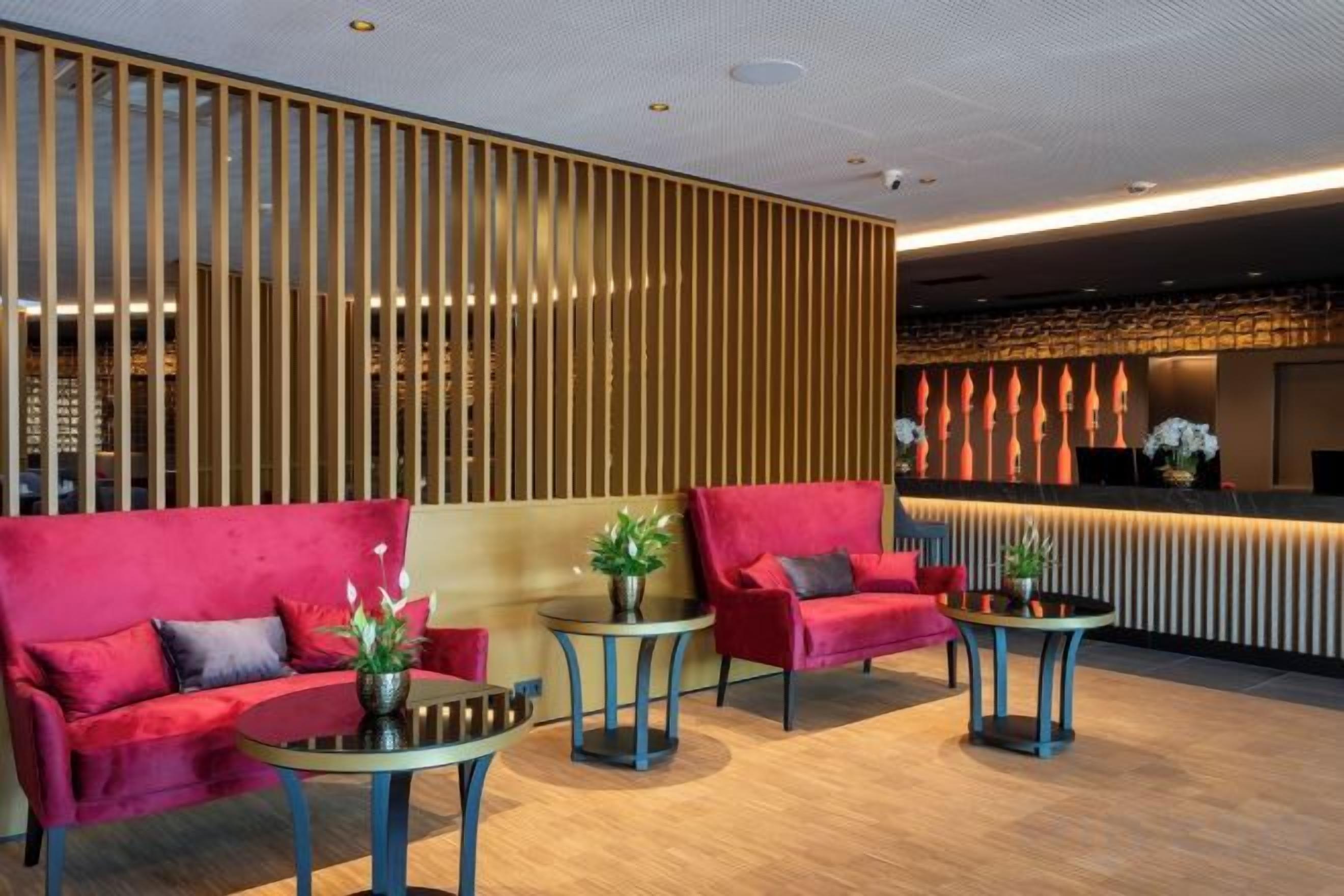 A modern lobby with red sofas, small round tables, and a wooden partition.