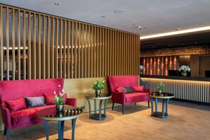 Een moderne lobby met rode banken, kleine ronde tafels en een houten scheidingswand.
