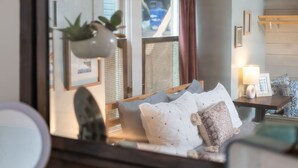 Une chambre avec un grand miroir, un lit avec de nombreux oreillers, une table de chevet avec une lampe et une fenêtre avec des rideaux.