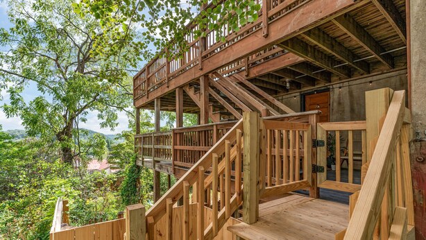 Un escalier en bois mène à une terrasse en bois d’où l’on peut admirer un paysage verdoyant et luxuriant.