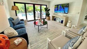 Un soggiorno con divano, tavolino, televisore e vista su una piscina.