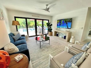 A modern living room with a blue sofa, a coffee table, and a TV on a wooden stand. - 677 Mod Beach Bliss | Heated Pool & Spa (Naples)