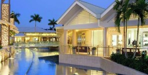 A hotel with a swimming pool, a covered walkway, and palm trees. - 677 Beach Break ·Beautiful 3/3 Home w/ Heated Pool (Naples)
