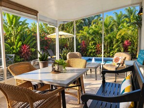 A covered outdoor seating area with wicker furniture, a table, and a view of a pool and tropical plants. - 677 Beach Break ·Beautiful 3/3 Home w/ Heated Pool (Naples)