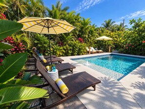 A pool area with lounge chairs and umbrellas, surrounded by tropical plants. - 677 Beach Break ·Beautiful 3/3 Home w/ Heated Pool (Naples)