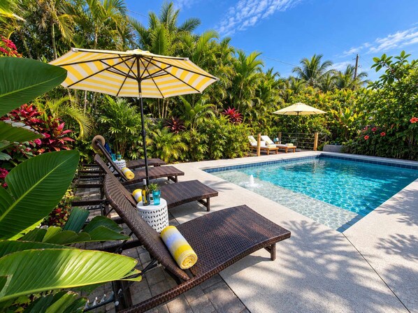 A pool area with lounge chairs and umbrellas, surrounded by tropical plants. - 677 Beach Break ·Beautiful 3/3 Home w/ Heated Pool (Naples)
