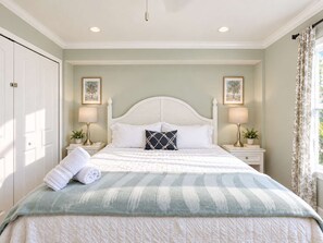 A bedroom with a bed, two bedside tables, a nightstand, a window with curtains, and a door. - 677 Beach Break ·Beautiful 3/3 Home w/ Heated Pool (Naples)