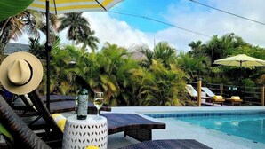 A poolside area with lounge chairs, a table with a bottle and glass, and a large umbrella. - 677 Beach Break ·Beautiful 3/3 Home w/ Heated Pool (Naples)