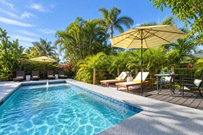 A swimming pool with lounge chairs and umbrellas, surrounded by tropical plants. - 677 Beach Break ·Beautiful 3/3 Home w/ Heated Pool (Naples)