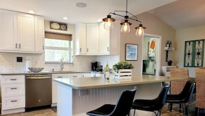 A modern kitchen with white cabinets, a central island with bar stools, and pendant lighting. - 677 Beach Break ·Beautiful 3/3 Home w/ Heated Pool (Naples)