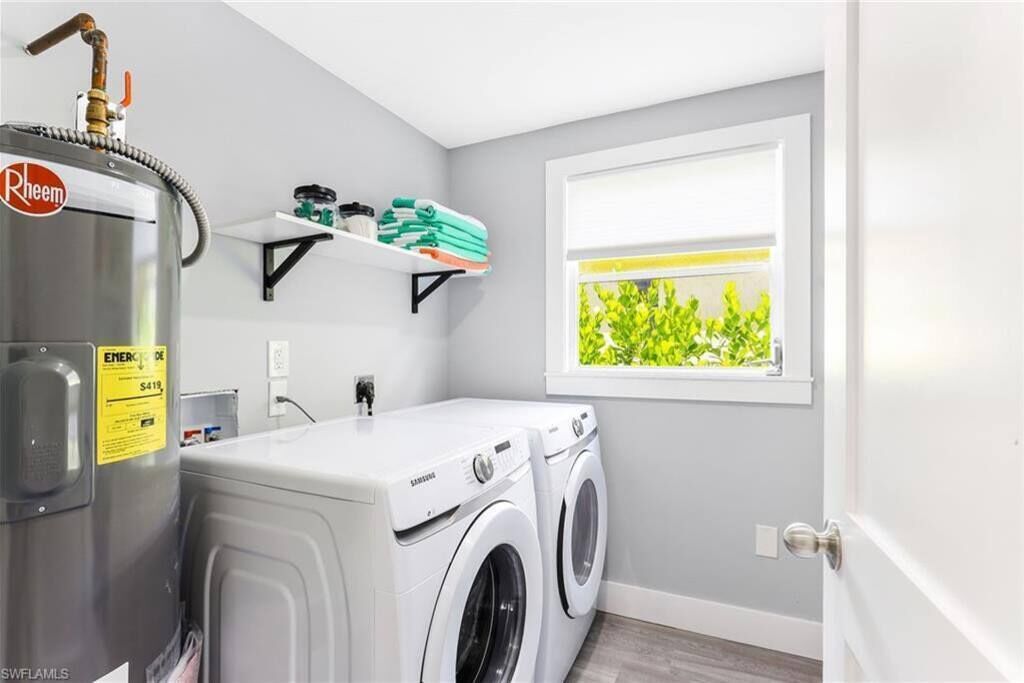 Une buanderie équipée d’un lave-linge et d’un sèche-linge, d’un chauffe-eau et d’une fenêtre donnant sur un espace verdoyant.