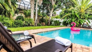 Un área de piscina con sillas de descanso, una mesa de vidrio y un flotador con forma de flamenco.