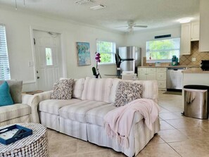 A living room with a sofa, a coffee table, and a kitchen area with a refrigerator and cabinets. - 563 Park Place | Bougain"Villa" | Mins to Beaches (Naples)