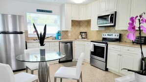 Una cocina moderna con armarios blancos, electrodomésticos de acero inoxidable, una mesa de comedor de vidrio y sillas blancas.