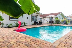 A swimming pool with a pink flamingo float, surrounded by a brick patio and white fences. - 563 Park Place | Bougain"Villa" | Mins to Beaches (Naples)