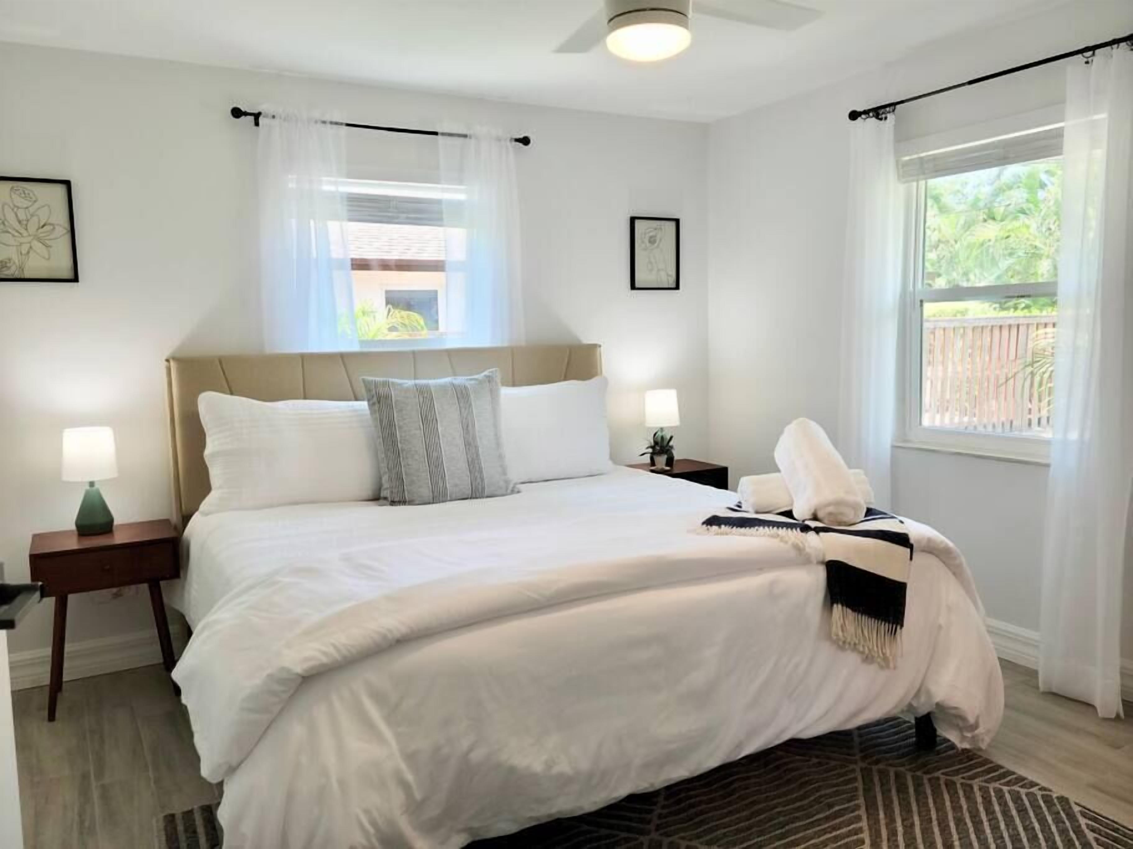 A neatly made bed with white linens, a bedside lamp, and a small table with a plant.