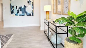 Un interior moderno con un cuadro abstracto grande, una consola con una lámpara y una planta en maceta.