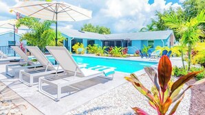A pool area with lounge chairs, a swimming pool, and a building with a blue roof. - 835 Villas of GulfShore | Walk 2 Mercato & Beaches (Naples)
