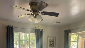 Ein Schlafzimmer mit einem Bett, einem Deckenventilator und einem Fenster mit Vorhängen.