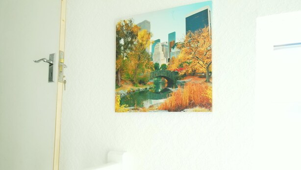 A door with a metal handle and a keyhole, a white door frame, and a painting of a bridge over a pond with autumn foliage and buildings in the background. - Stylish 2 Bed Room Apartment 3 Sleep Free Wifi & p (Newport)