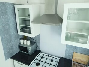 Una cocina con estufa a gas, microondas y alacenas con vajilla.