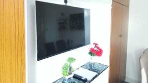 A room with a mounted flat-screen TV, a small table with a vase of flowers, and wooden cabinets. - Stylish 2 Bed Room Apartment 3 Sleep Free Wifi & p (Newport)